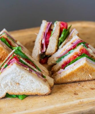 Tasty club sandwich with fresh ingredients on a wooden board, perfect for a quick meal.