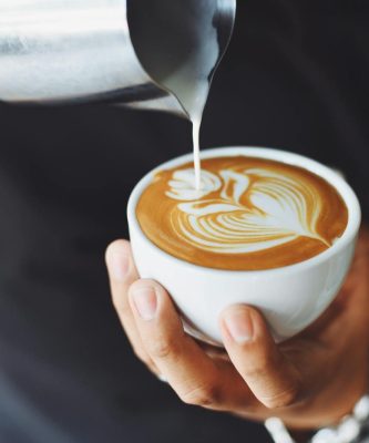 Close-up of a barista pouring milk to create latte art in a coffee cup.