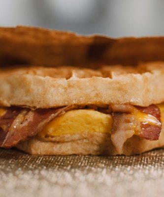Mouthwatering waffle sandwich with bacon, egg, and cheese wrapped in paper.